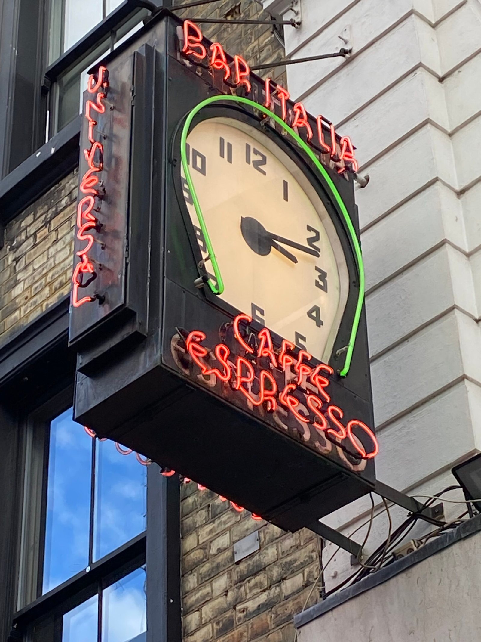 Historic photo snippet of the iconic Bar Italia neon clock sign in Soho, London, glowing with red and green neon illumination, representing the 40-year signage maintenance legacy of Moderneon.